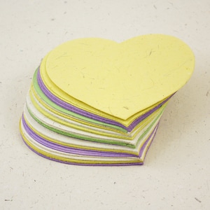 May include: A stack of heart-shaped paper cutouts in shades of yellow, green, purple, and white. The paper is textured and has a handmade look.