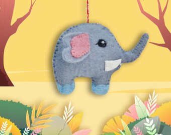 May include: A gray felt elephant ornament with pink ears and white tusks hanging from a red string against a yellow background with green foliage.