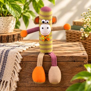 May include: A plush monkey toy with a cylindrical body featuring horizontal olive green and brown stripes. It has a white face, googly eyes, a small orange and green plaid bow tie, orange hands, and mismatched legs in tan and purple.