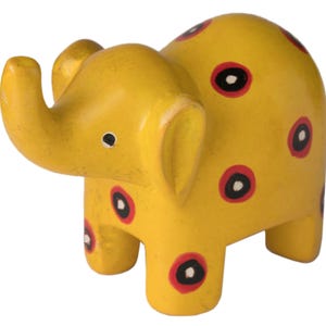 May include: A small yellow elephant figurine with red and black polka dots. The elephant is standing on all four legs and has a raised trunk.