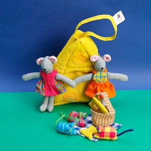 May include: A set of plush gray mice with colorful dresses and a yellow felt house. The mice are holding a picnic basket with a yellow lunchbox and a red and white checkered blanket. There are also four smaller mice with colorful patterns.