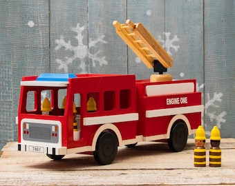May include: A red wooden toy fire truck with a ladder, four windows, and the words "Engine One" on the side. The truck has black wheels and a blue light on top. Three small wooden figures with yellow hats are standing in front of the truck.