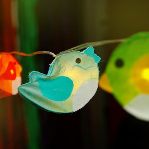 May include: A string of fairy lights with paper bird and fish shapes. The bird is blue with white accents and the fish is green with yellow accents.