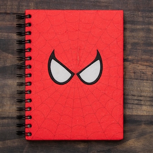May include: Red spiral notebook with a black and white spider-man mask design on the front cover.