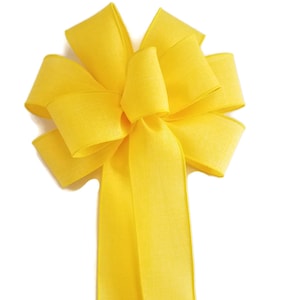 May include: A large, bright yellow bow made from satin ribbon. The bow has a long tail and is tied in a classic, symmetrical style.