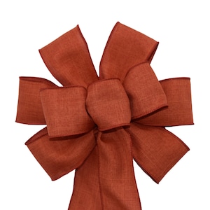May include: A large, rust-colored bow made from a textured fabric. The bow is tied with a long tail.