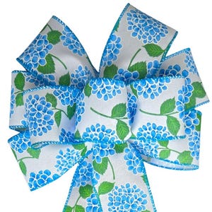 Può includere: Un fiocco blu e bianco con una stampa floreale di ortensie. Il fiocco è fatto di nastro e ha un bordo con filo.