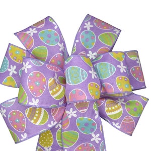 May include: A purple Easter bow with a pattern of colorful eggs and white flowers. The bow is made of a soft, textured fabric.