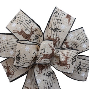 May include: A brown and beige Christmas bow with a musical note and reindeer design. The bow is made of burlap and has a black trim.
