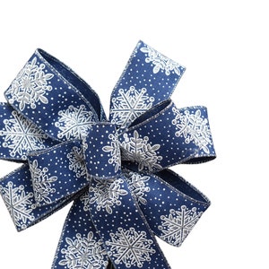 May include: A blue and white ribbon bow with a snowflake pattern. The bow is tied in a classic shape with loops and tails.