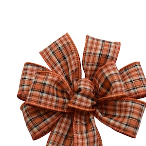 May include: A large, orange and white plaid bow. The bow is made of a soft, woven fabric with a subtle sheen.