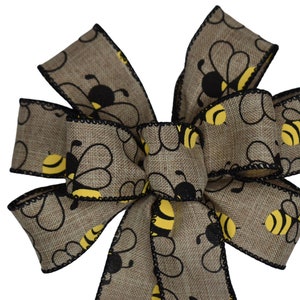 May include: A brown burlap ribbon bow with a black and yellow bee pattern. The bow is tied with a black ribbon and has a frayed edge.