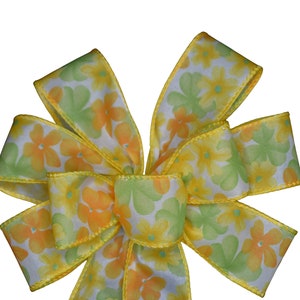 May include: A yellow and green floral ribbon bow with a white background. The bow is tied in a classic shape with the ends of the ribbon flowing out.