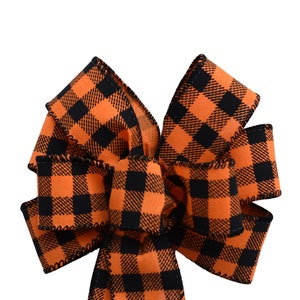 May include: A large orange and black plaid bow. The bow is made of a thick, woven fabric with a black stitched edge.