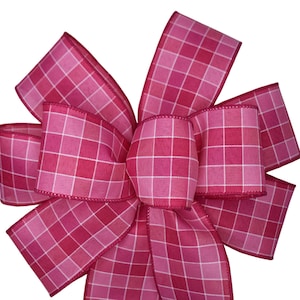 May include: A pink and white plaid bow with a large, centered knot. The bow is made of a soft, textured fabric.