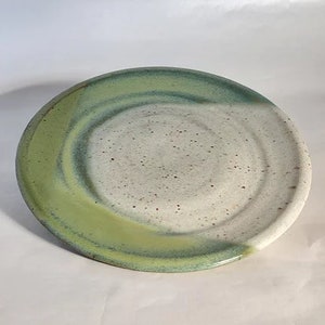 May include: A white ceramic plate with a green glaze on the rim. The glaze is uneven, creating a mottled effect.