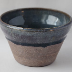 May include: A small, dark blue ceramic bowl with a speckled brown glaze on the bottom. The bowl has a rounded shape and a slightly flared rim.