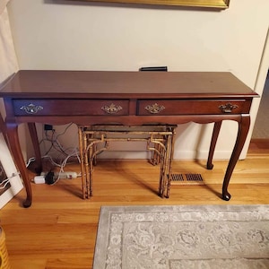 May include: A dark brown wooden console table with two drawers and a gold-painted bamboo nesting table underneath. The table has a simple, elegant design with curved legs.