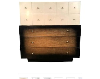 May include: A vintage dresser with a white top section with multiple drawers and a lower section with three drawers. The lower drawers are made of wood with a dark brown stain and a black finish.