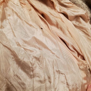 May include: Close-up of the inside of a beige jacket, showing the lining made of a soft, peach-colored fabric.