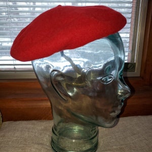 May include: A red felt beret on a glass mannequin head.