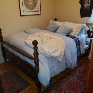 May include: A wooden bed frame with a light blue bedspread and white blanket. The bed has a headboard and footboard with decorative posts. There are blue and white patterned pillows on the bed.