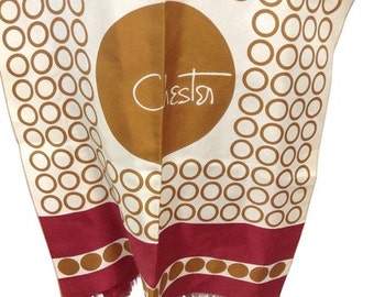Può includere: Un foulard di seta bianco con un cerchio marrone al centro. Il cerchio ha la parola "Chester" scritta in un font corsivo. Il foulard ha un bordo rosso con un motivo marrone.