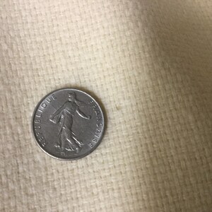 May include: A silver French coin with the inscription "REPUBLIQUE FRANCAISE" and a depiction of a woman walking.
