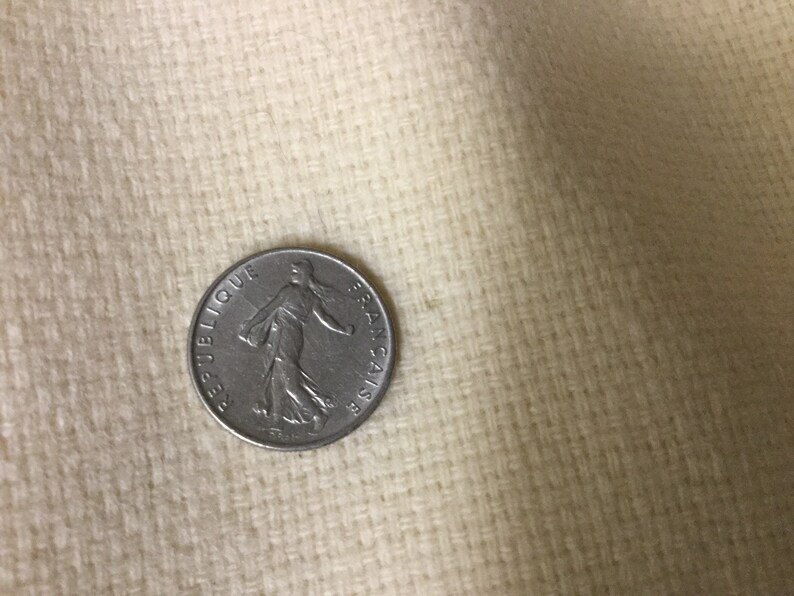 May include: A silver French coin with the inscription "REPUBLIQUE FRANCAISE" and a depiction of a woman walking.