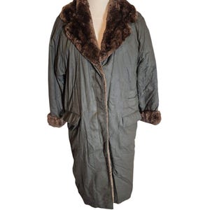 May include: A long, dark green coat with a brown faux fur collar and cuffs. The coat has a button closure and two pockets.