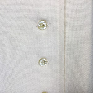 May include: Close-up of a white fabric with two white buttons. The fabric has a woven texture.