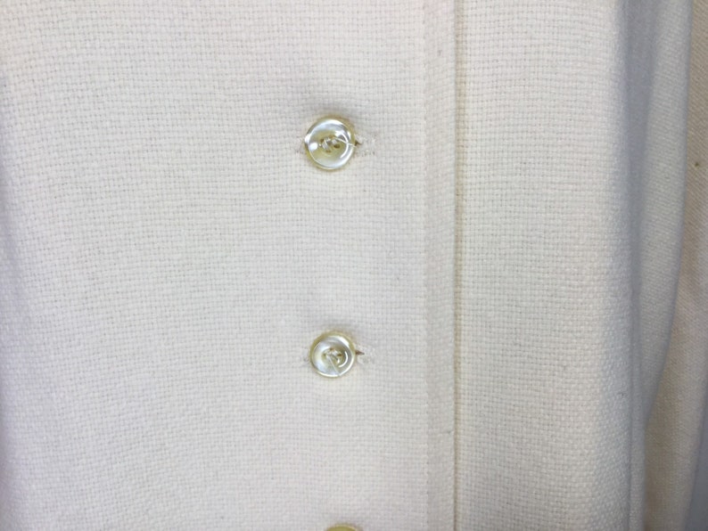 May include: Close-up of a white fabric with two white buttons. The fabric has a woven texture.