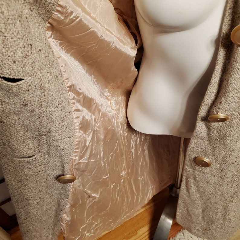 May include: A beige tweed coat with a double breasted closure and gold buttons. The coat is lined with a silky, peach-colored fabric.