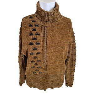 May include: A brown turtleneck sweater with black semi-circle cutouts and vertical black lines. The long-sleeved sweater is displayed on a white mannequin. The sweater has a ribbed texture and a relaxed fit.
