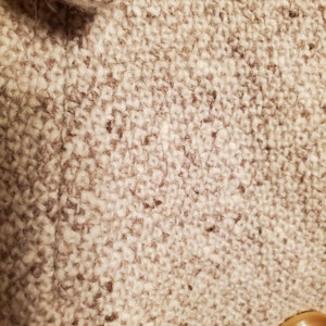 May include: Close-up of a beige tweed fabric with a subtle brown herringbone pattern. The fabric has a soft, fuzzy texture.