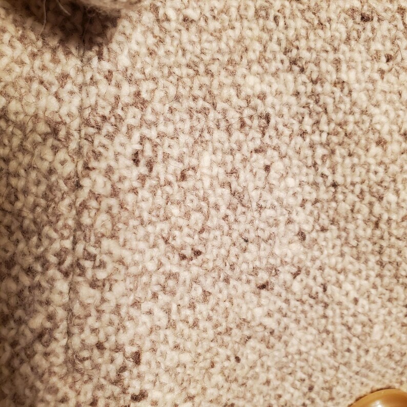 May include: Close-up of a beige tweed fabric with a subtle brown herringbone pattern. The fabric has a soft, fuzzy texture.