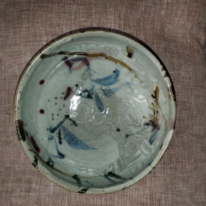May include: A white ceramic bowl with a blue, brown, and red abstract design. The bowl has a slightly uneven rim and a smooth, glazed interior.