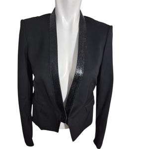 May include: A black blazer with a textured lapel and a tailored fit. The blazer is displayed on a white mannequin, showcasing its design and structure. The lapel has a snakeskin pattern.