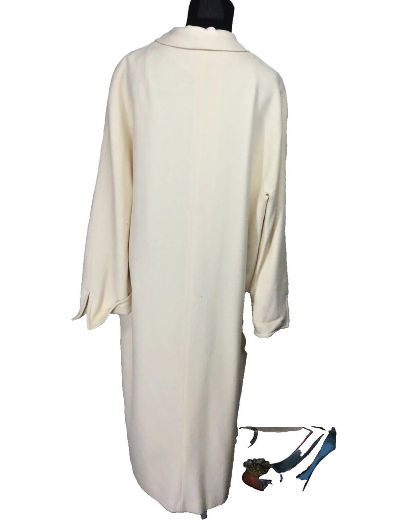 May include: A long, off-white coat with a simple design and long sleeves. The coat is made of a soft, textured fabric.