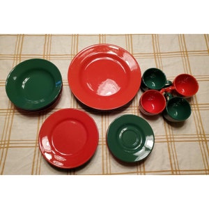 Può includere: Un set di stoviglie in ceramica rossa e verde, che comprende piatti e tazze. I piatti hanno una finitura lucida e le tazze hanno un manico.
