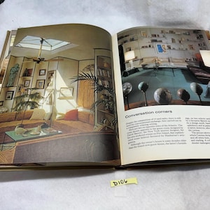 Puede incluir: Un libro abierto con imágenes de diseño de interiores. Una página muestra una sala de estar con tragaluz, asientos empotrados y obras de arte. La página opuesta tiene el titular "Conversation corners" y texto sobre el diseño de la habitación.