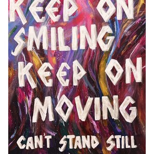 May include: A rectangular canvas painting featuring a vibrant, multi-colored abstract background with swirling strokes of purple, red, blue, and gold. The white, block-lettered text reads: KEEP ON SMILING KEEP ON MOVING CAN'T STAND STILL @ANNIEMGO.