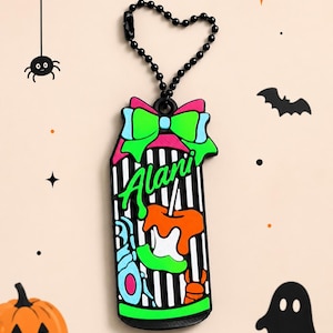 May include: A rubber keychain featuring a black and white striped can design with a bright neon green bow on top. The word Alani is written in green script across the center, accompanied by orange and blue graphic accents of candy and treats.