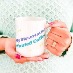 May include: White ceramic coffee mug with the text "My Dissertation Wanted Coffee" in blue and purple lettering with yellow stars.