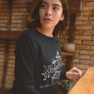 Op de afbeelding: Zwart sweatshirt met een witte afbeelding van twee motten en bladeren. De tekst "Ad astra per aspera" is onder de afbeelding gedrukt.