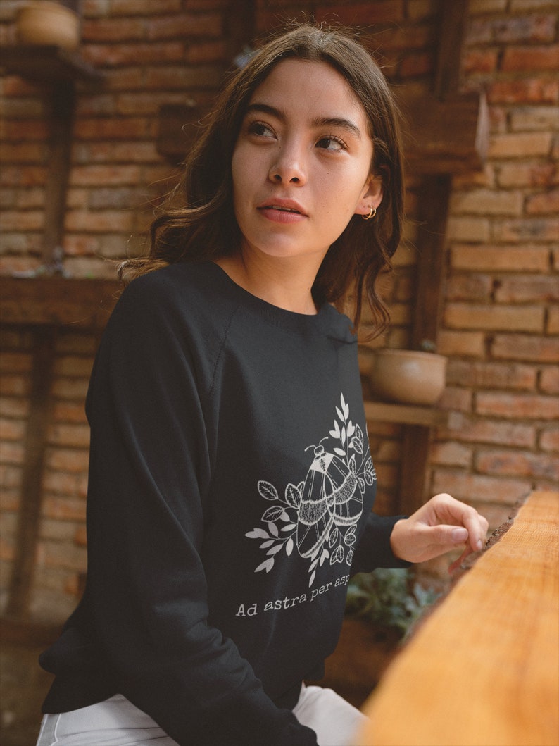 Op de afbeelding: Zwart sweatshirt met een witte afbeelding van twee motten en bladeren. De tekst "Ad astra per aspera" is onder de afbeelding gedrukt.