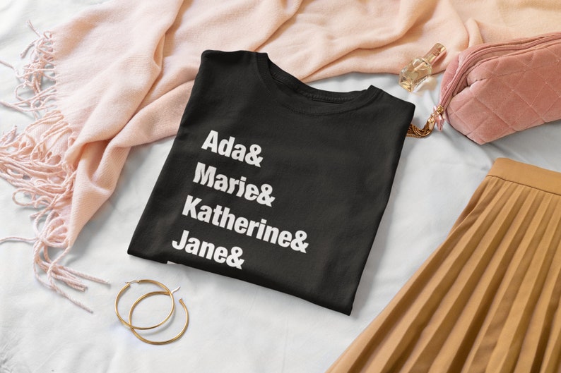 May include: Black t-shirt with white text that reads "Ada & Marie & Katherine & Jane &"