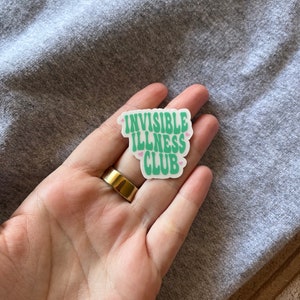 May include: A white sticker with the text "Invisible Illness Club" in green letters with pink hearts on either side of the text.
