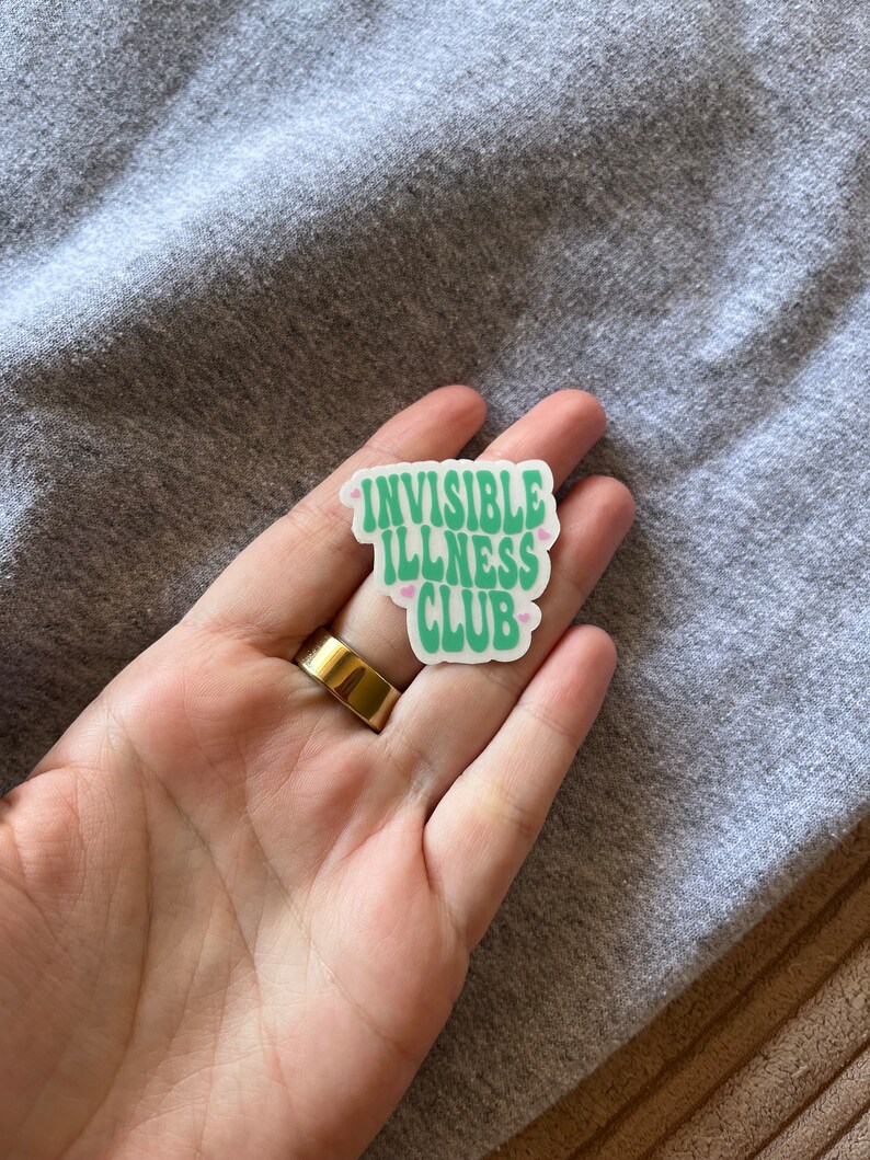 May include: A white sticker with the text "Invisible Illness Club" in green letters with pink hearts on either side of the text.