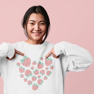 May include: A white sweatshirt with a heart-shaped design made up of pink and green strawberries.